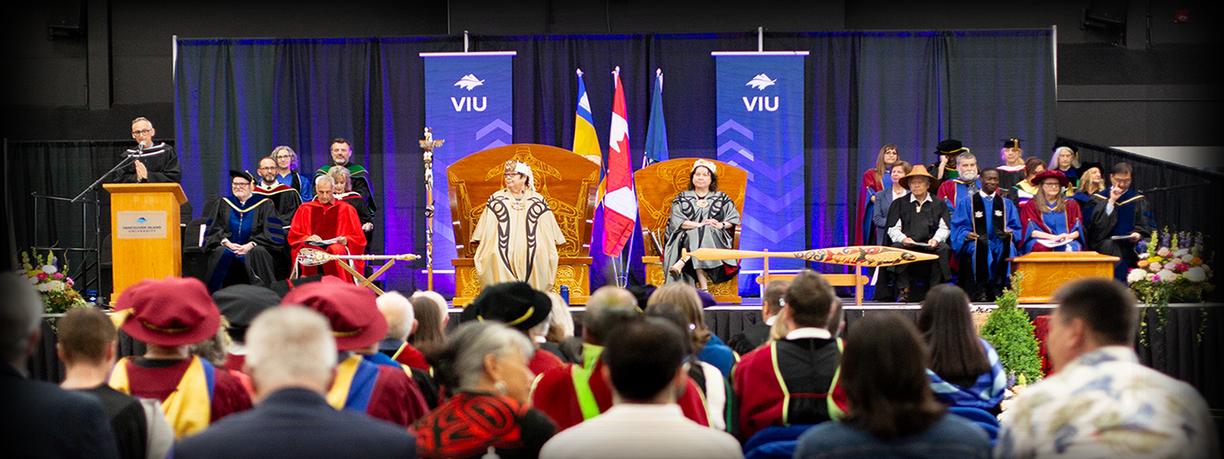 Gowned dignitaries on a stage amid Indigenous ceremonial pieces