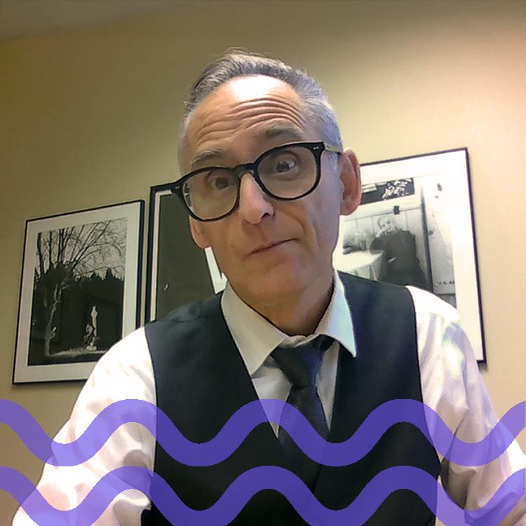 Man with dark glasses wearing a vest and tie with a purple wave pattern