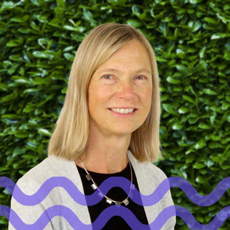 Smiling woman with blond hair and wearing a white cardigan with a purple wave pattern