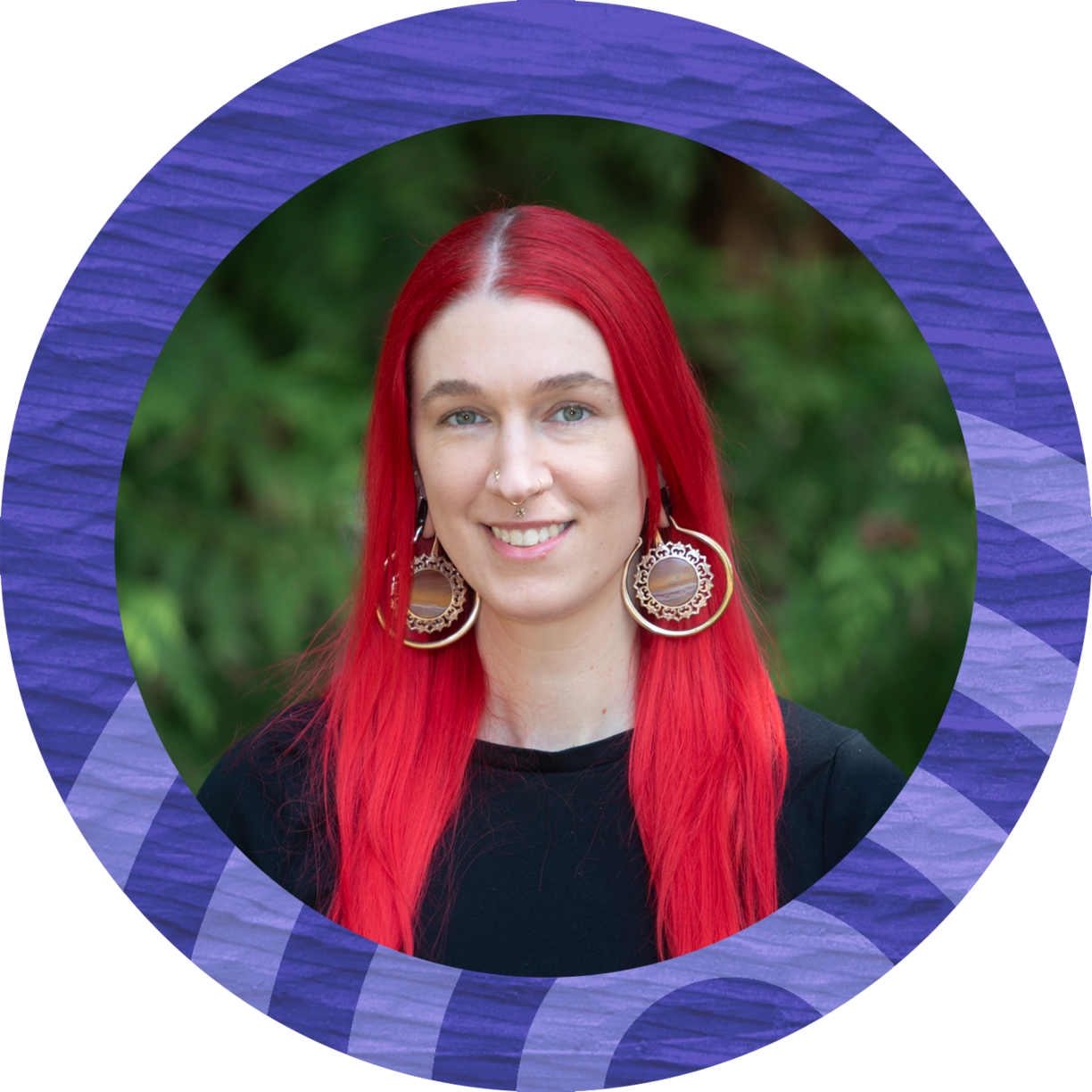 Young woman with bright red hair and a dark top standing in front of trees