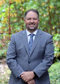 A man in a suit in front of greenery.