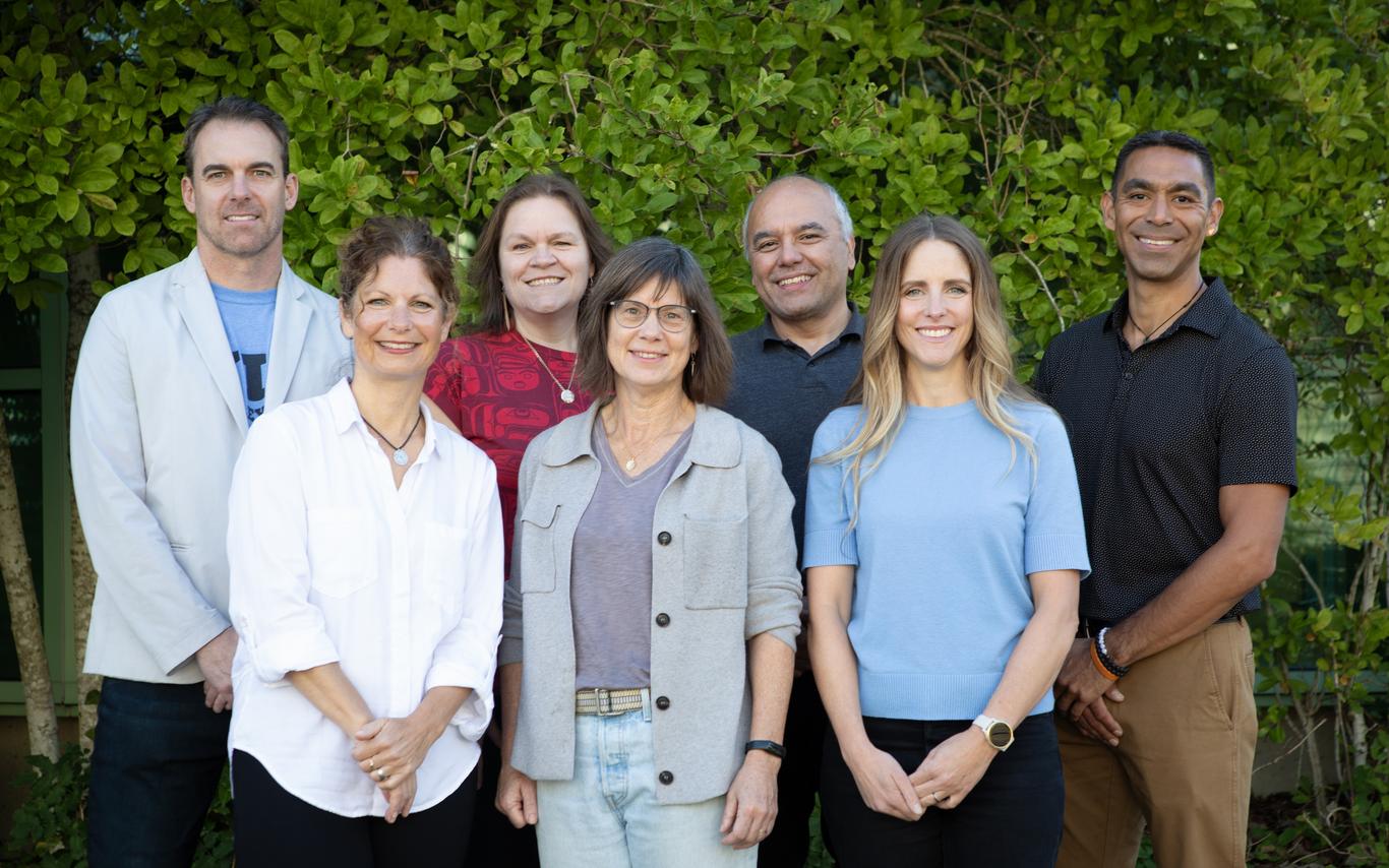 Smiling men and women standing together in front of bushes